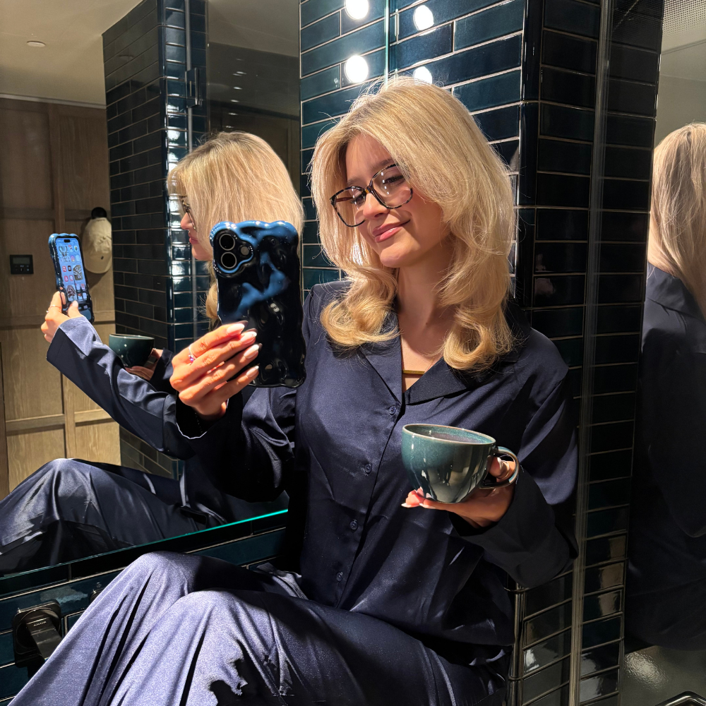 Woman in navy pajamas smiles in a mirror selfie holding a blue 3D bubble-textured phone case.