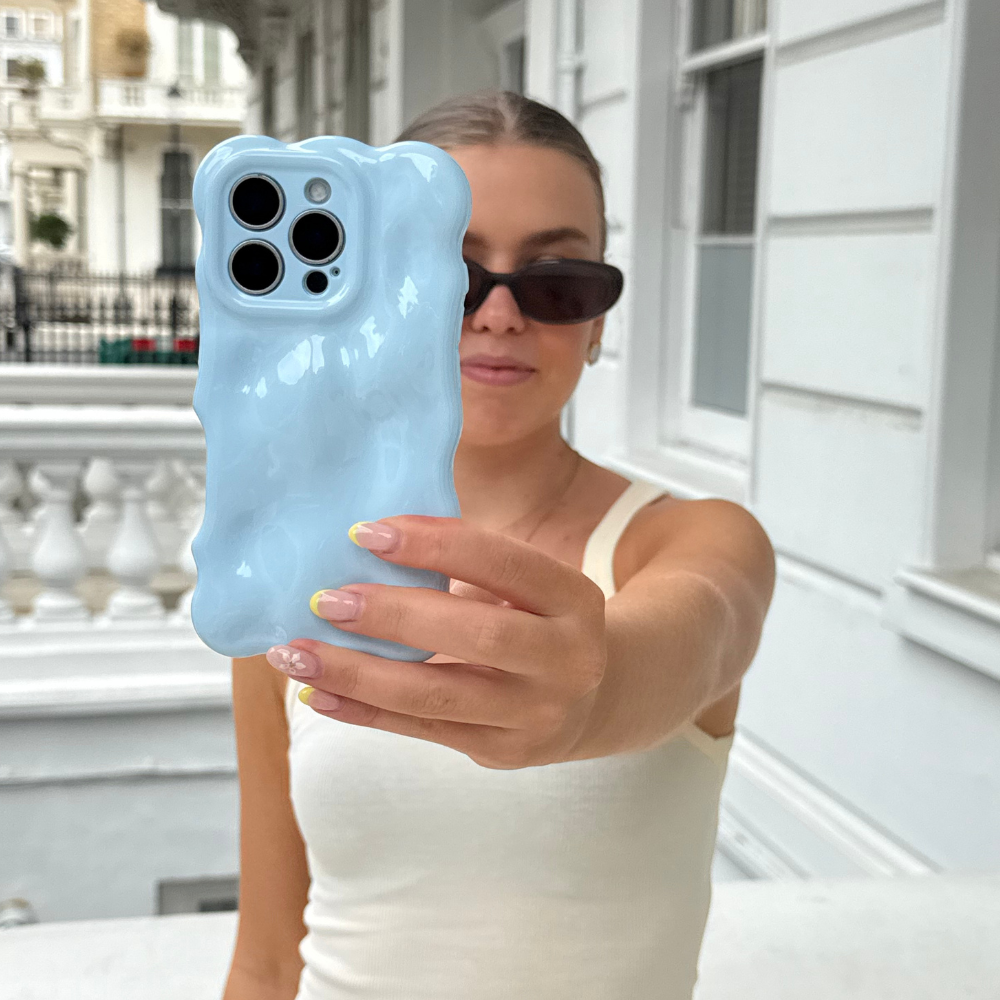 Woman outdoors in a white tank top holds phone with Coconut Lane 3D Bubble Case in light blue.