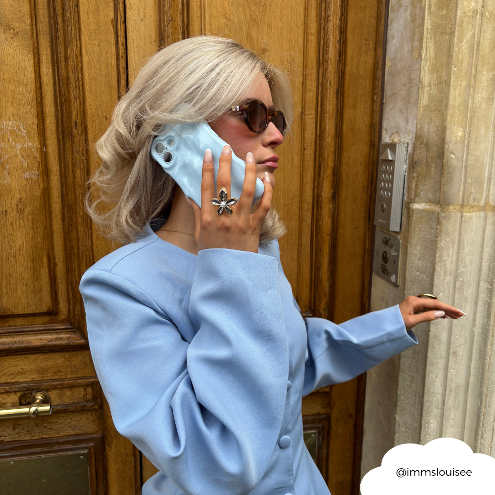 Woman in blue blazer holding phone with Coconut Lane 3D Bubble Baby Blue case outdoors.
