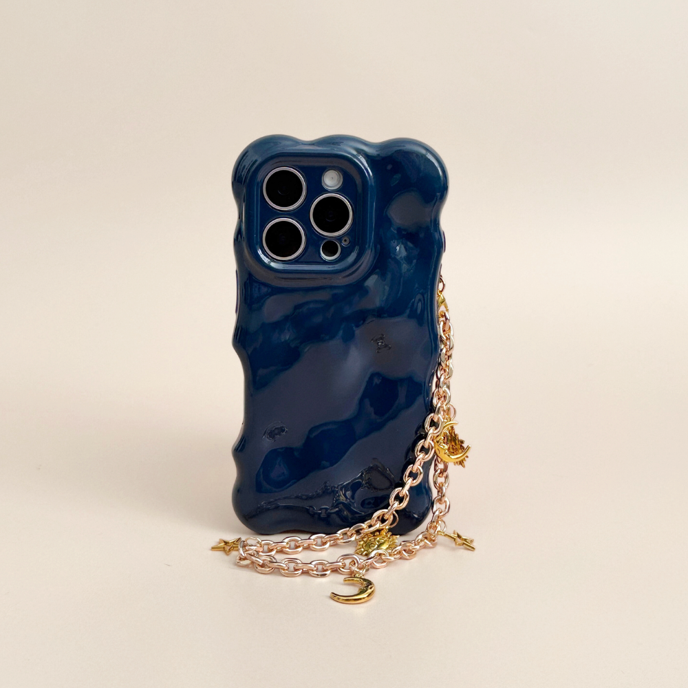 Glossy navy wavy iPhone case with gold chain strap and celestial-themed phone strap decorated with stars, moons, and suns.