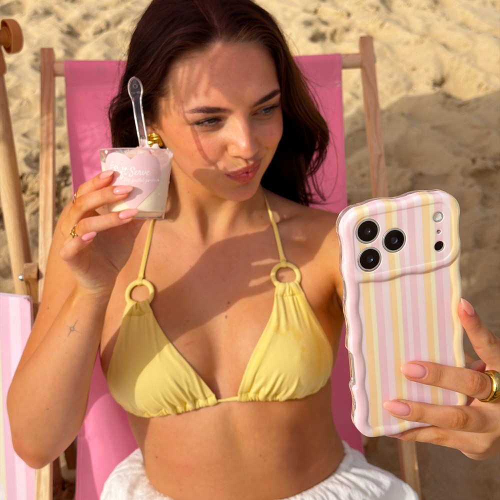 Girl posing on the beach with her ice cream in a pink deck chair taking a selfie with the Wavy Pastel Stripes Phone Case