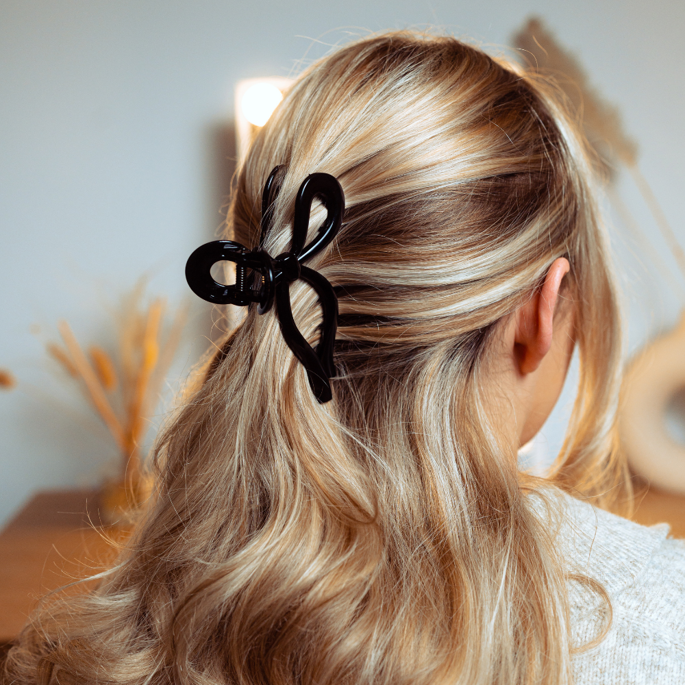 A person with blonde hair styled in a half-updo secured with a large black hair clip shaped like a bow.
