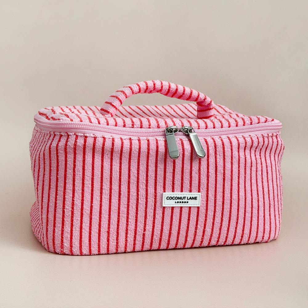 A pink and red striped fabric makeup bag with a handle and double zipper, labeled "Coconut Lane," sits on a neutral background.