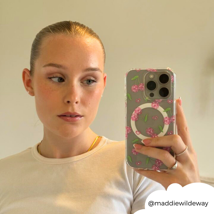 A person with light skin and straight, pulled-back hair takes a mirror selfie with the Clear MagSafe® Phone Case - Disco Cherries by Coconut Lane. They are wearing a white top and a gold necklace. The Instagram handle "@maddiewildeway" is seen in the corner of the image.