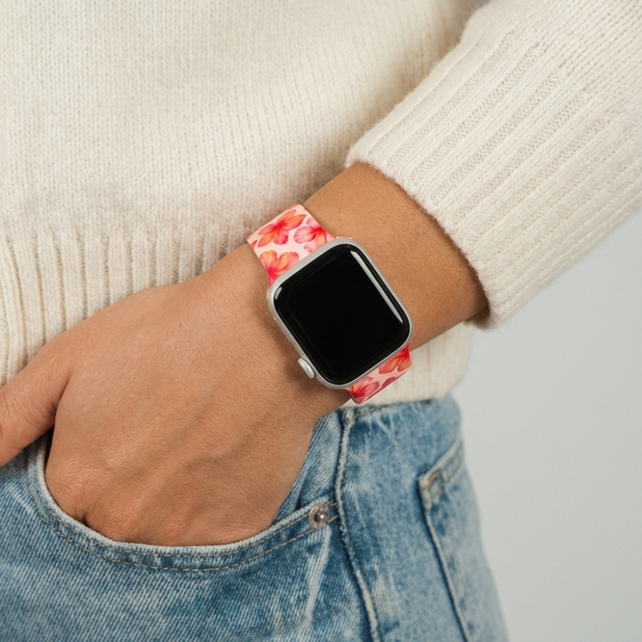 Pink hibiscus-patterned Apple Watch strap by Coconut Lane, worn with a cream sweater and blue jeans.