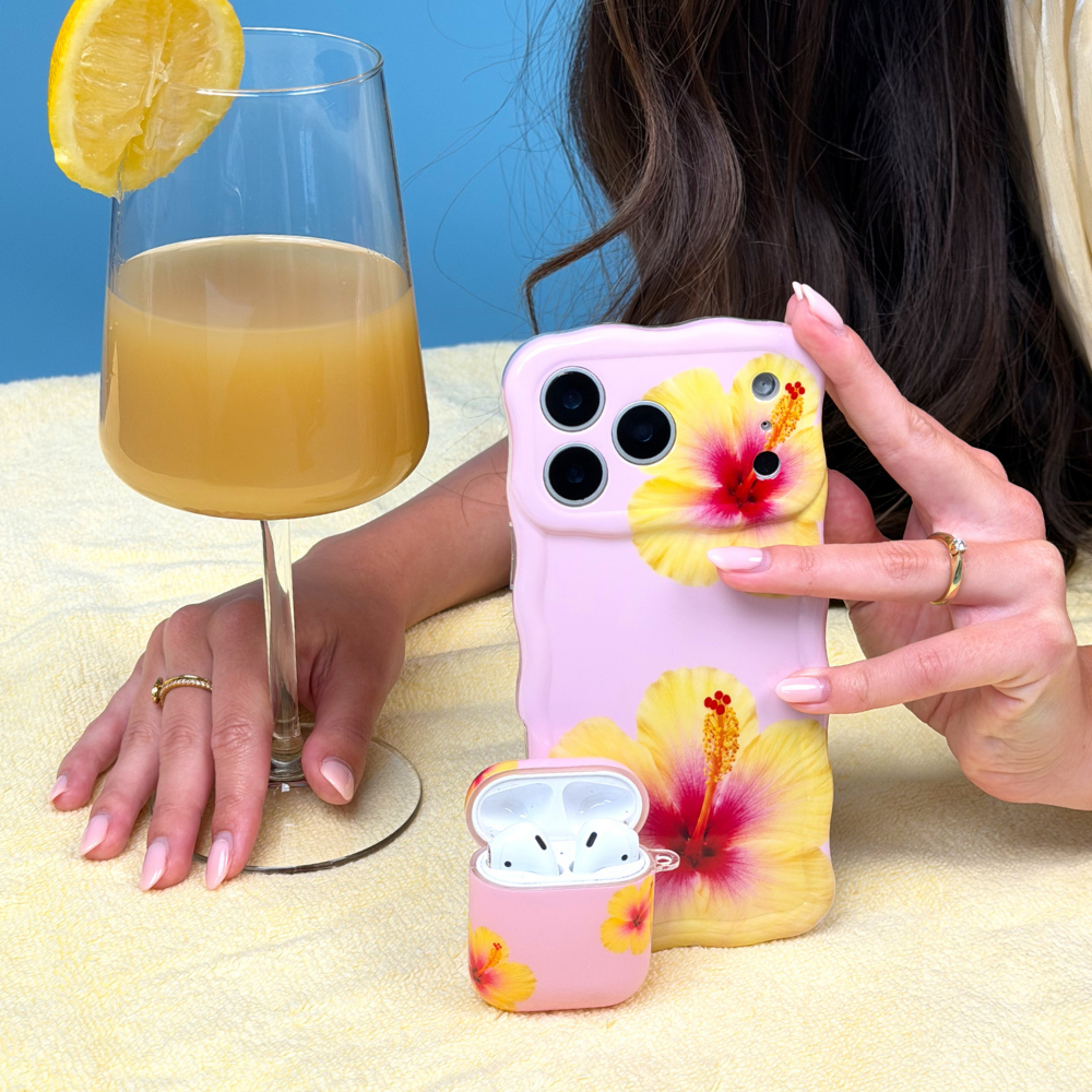 Person holding a phone with a floral case next to a glass of juice and airPods case.