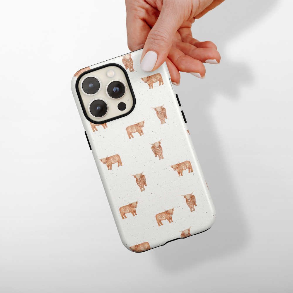 Hand holding a white Coconut Lane phone case with a brown highland cow pattern.