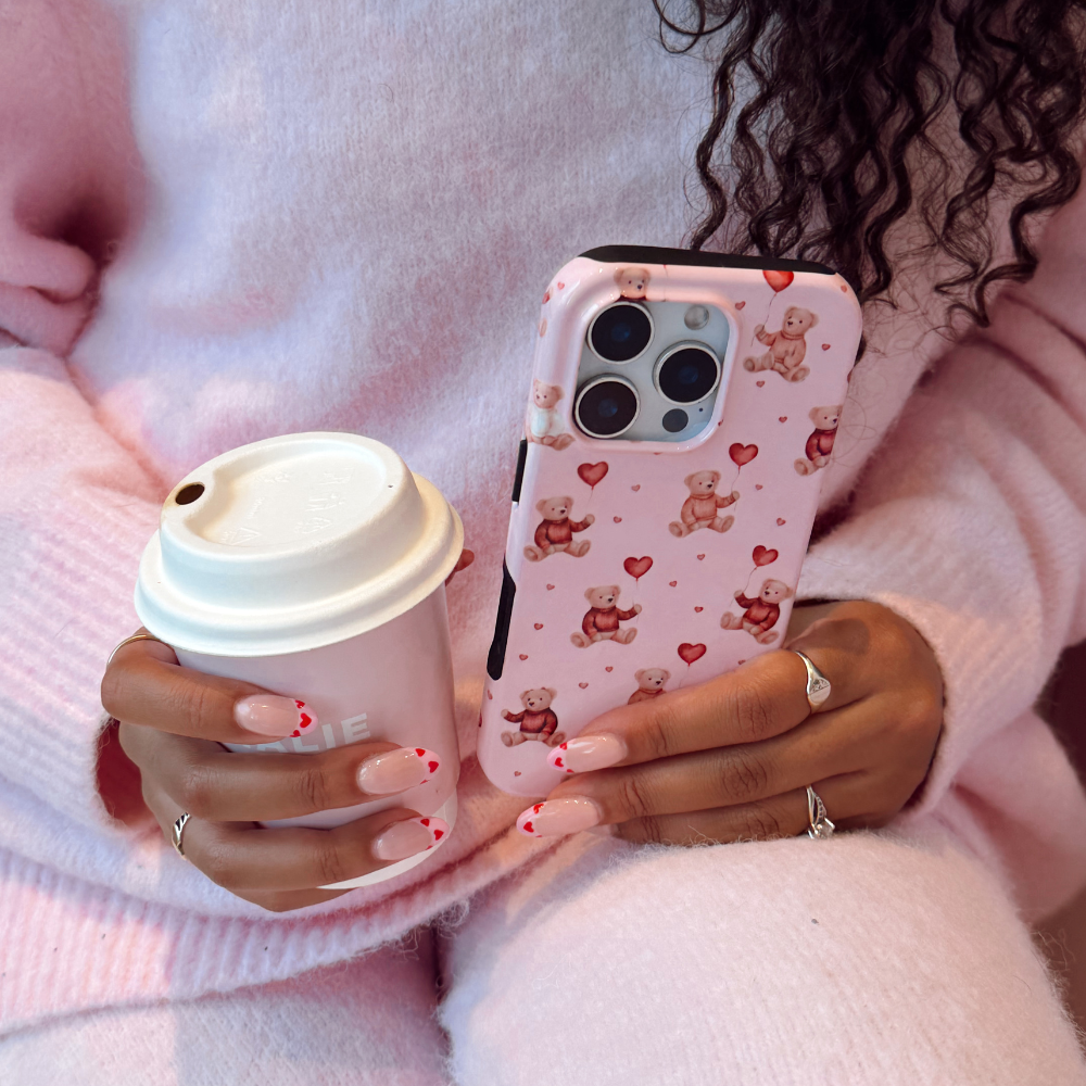 Person holding a coffee cup and a phone with a teddy bear case.