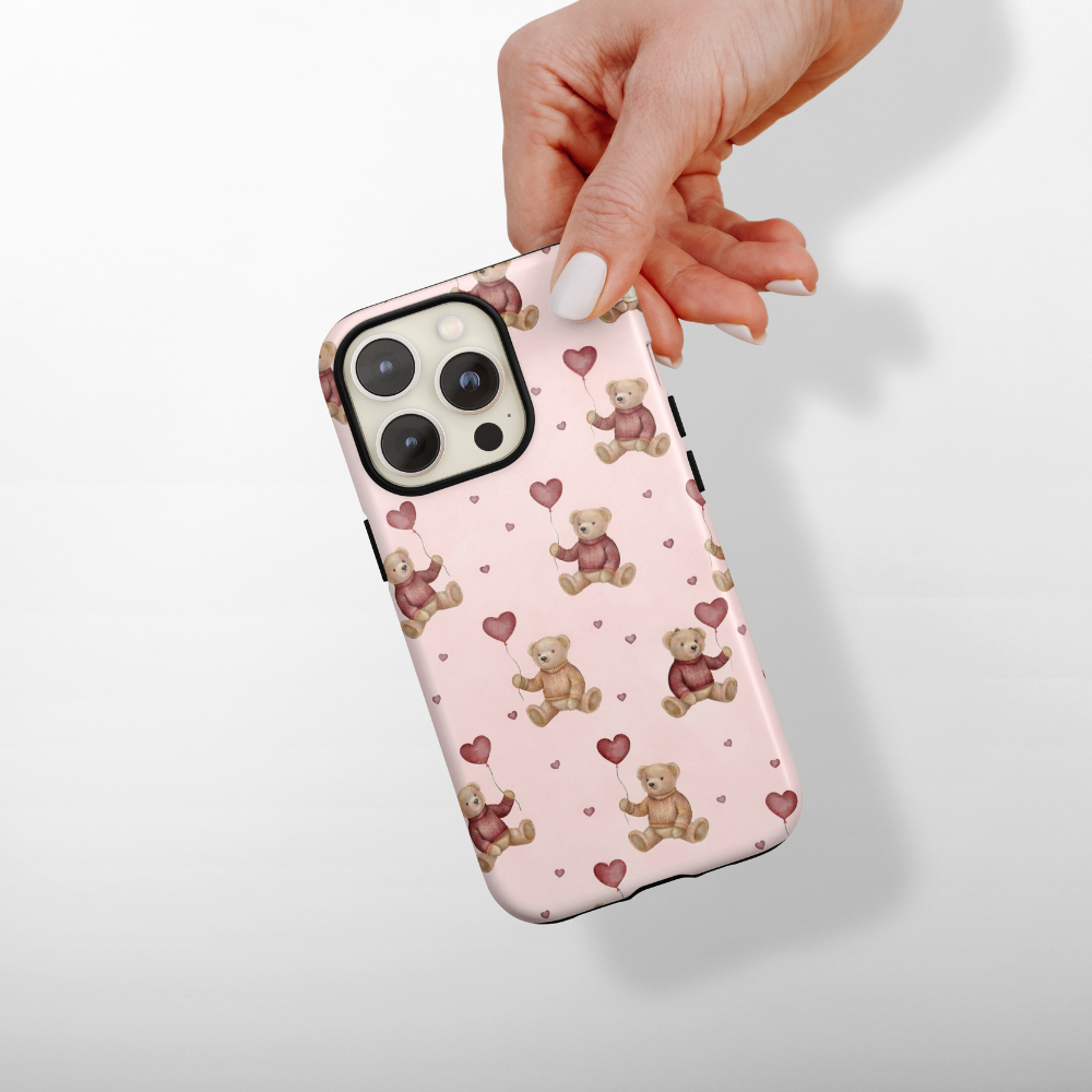 Phone case with teddy bear and heart pattern held by a hand on a light background