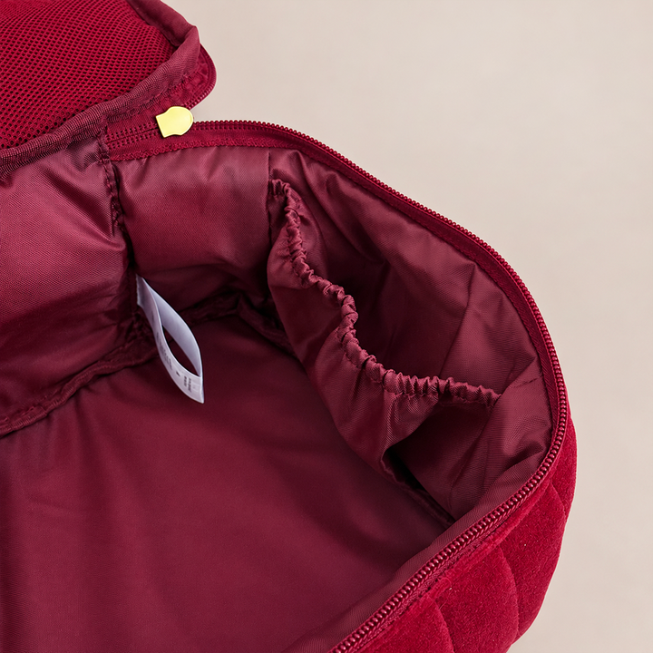 Close-up of the interior of a burgundy zippered bag or organizer, showing a padded lining, elastic pocket, zipper pull, and a small white tag on a light beige background.
