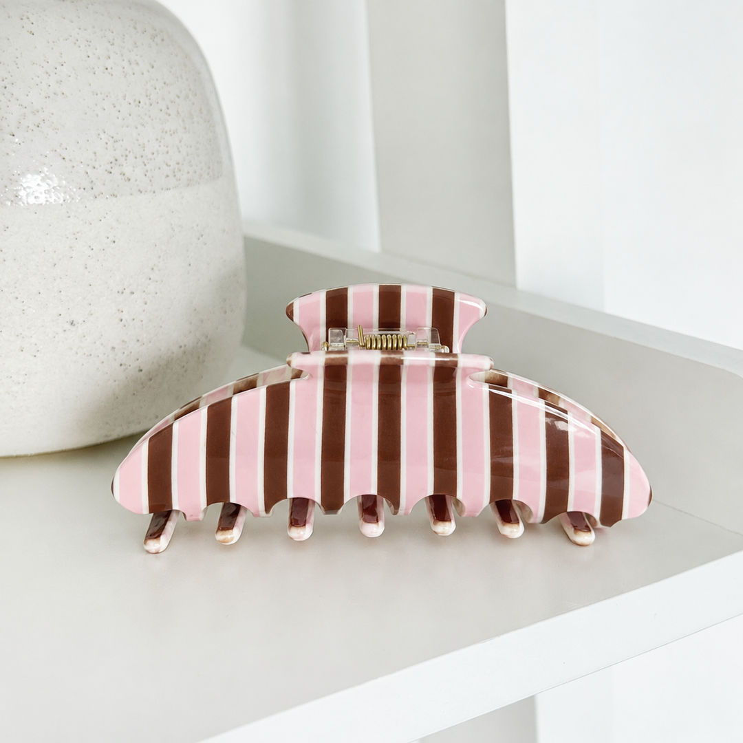 Claw Clip featuring glossy chocolate brown, blush pink and cream vertical stripes, with a gold-toned spring hinge and curved teeth, photographed on a white shelf.