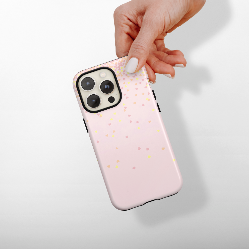 Hand holding a pink phone case with small colorful hearts on a light gray background