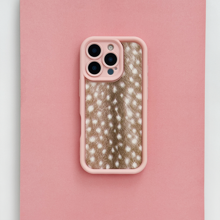 A phone case with pink edging and brown fawn-print center featuring white spots, shown on a phone against a solid pink background.
