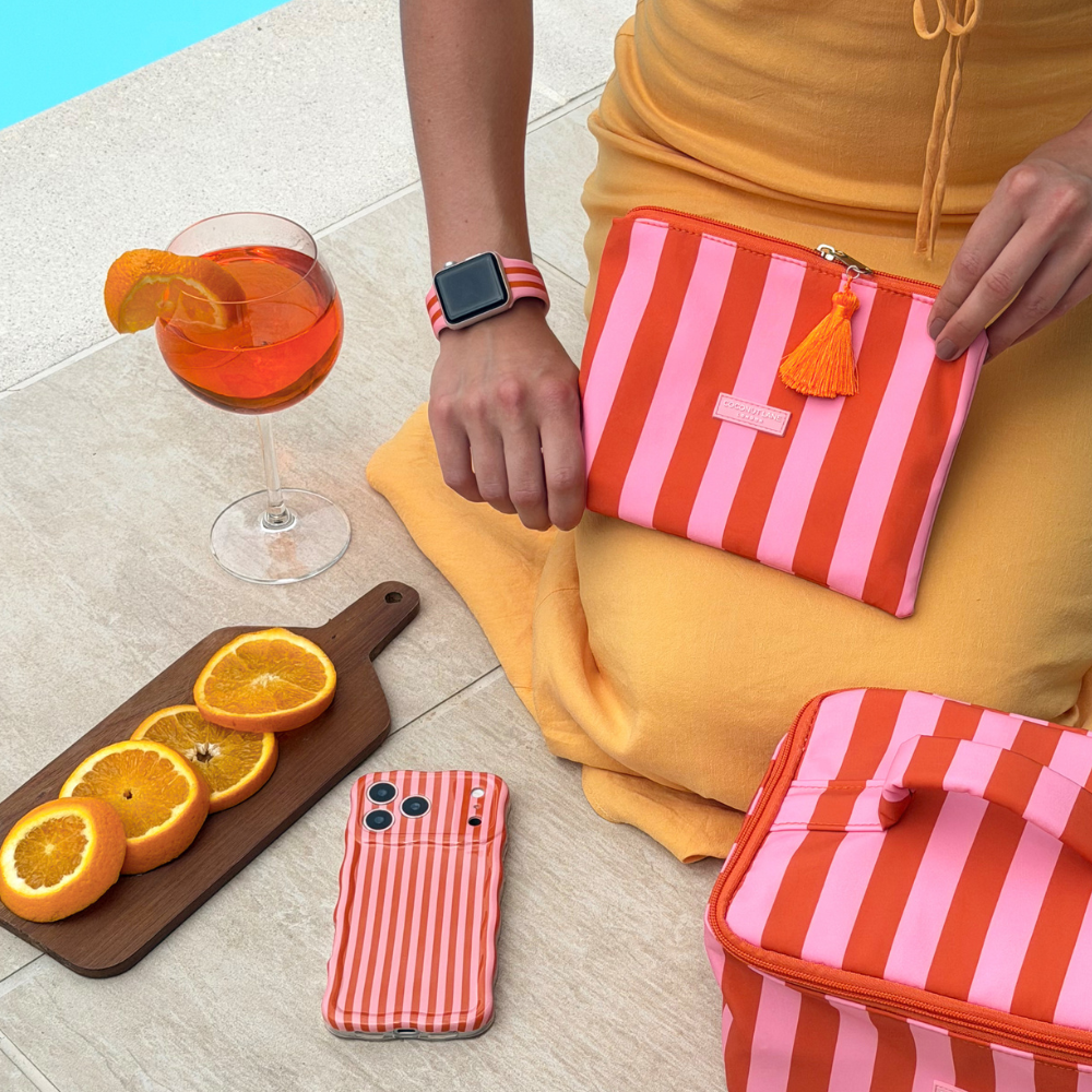 Person holding a mini striped pouch with a drink and fruit on a table