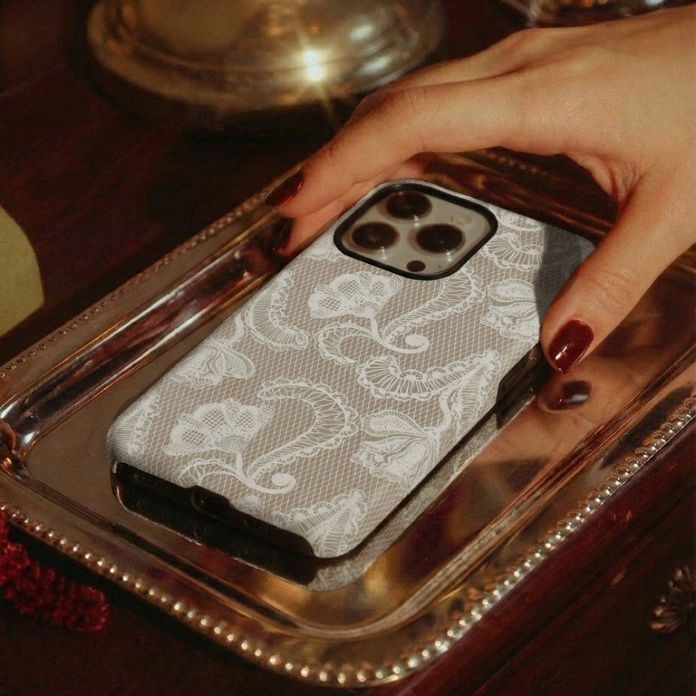 Phone case with lace design held by a hand on a reflective platter