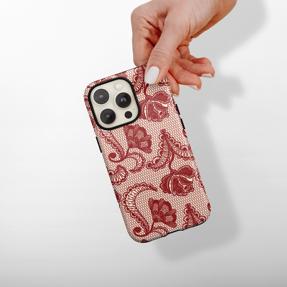 A hand holds a Coconut Lane tough iPhone case featuring a red floral lace design.
