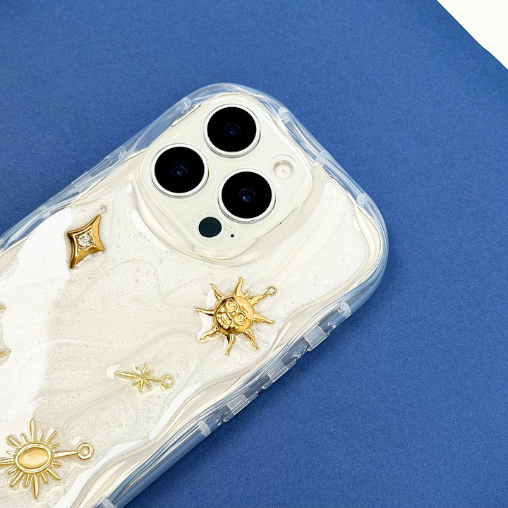 Stardust after dark charm phone case. A pearl base with luxe gold celestial charms including a moon, sun, star, diamond shape and 11:11 charm. 