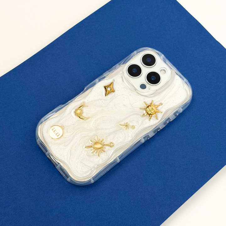 Stardust after dark charm phone case. A pearl base with luxe gold celestial charms including a moon, sun, star, diamond shape and 11:11 charm. 