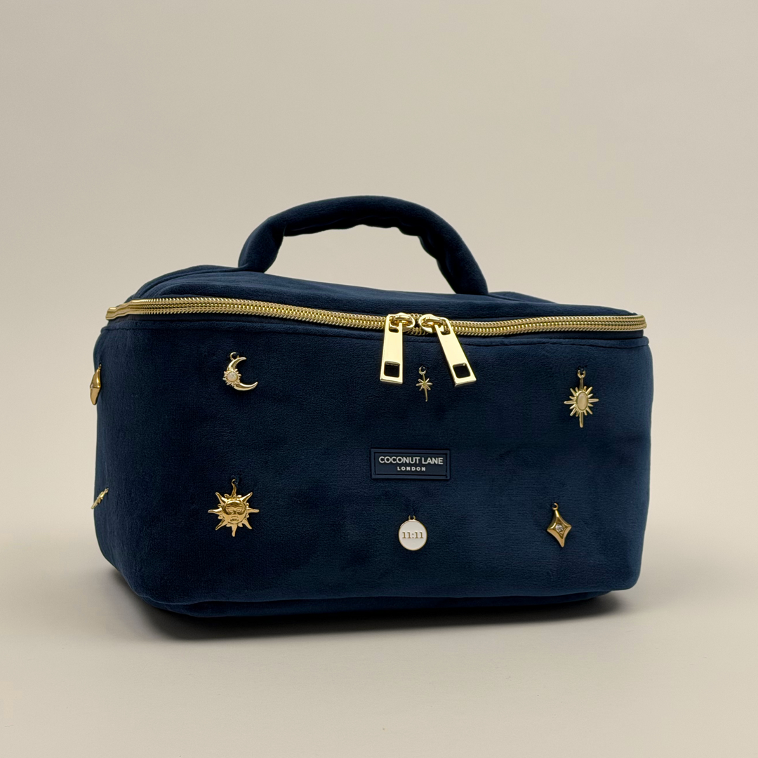 Stardust After Dark Vanity Case. A dark blue navy velvet vanity case with gold zip, and sewn-on gold celestial-themed charms. Including a moon, sun, star, diamond shape and 11:11 charm. 