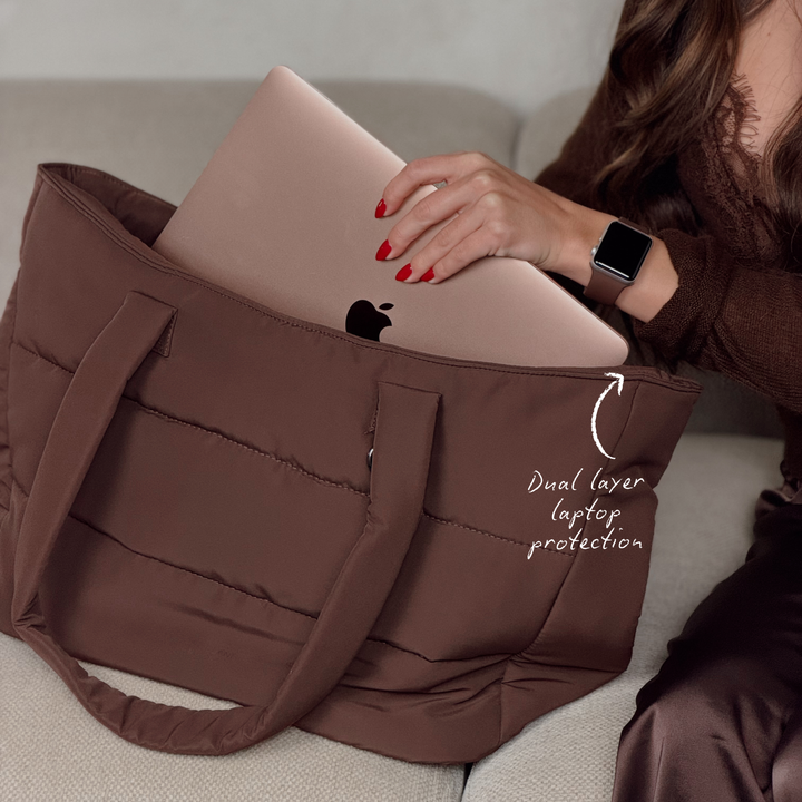 Close-up image of the Main Carry Choc Brown Puffer Bag showing the dual layer laptop protection compartment. On the woman's wrist is a Coconut Lane NAKD apple watch strap in chocolate brown. 