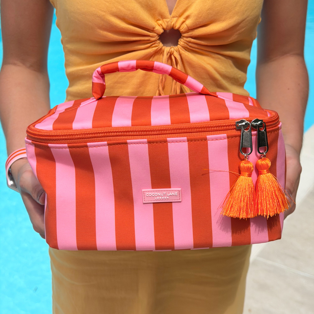 Person holding a orange and pink striped vanity case with tassels against a blue background