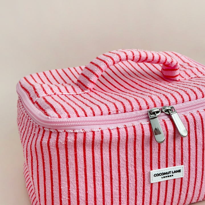 Pink and red striped makeup bag with Coconut Lane brand label on a beige background