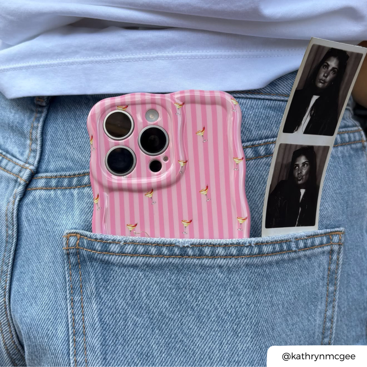Back pocket of blue jeans has wavy pink striped phone case with small spicy margarita illustrations poking out the top alongside a photobooth photo strip. 