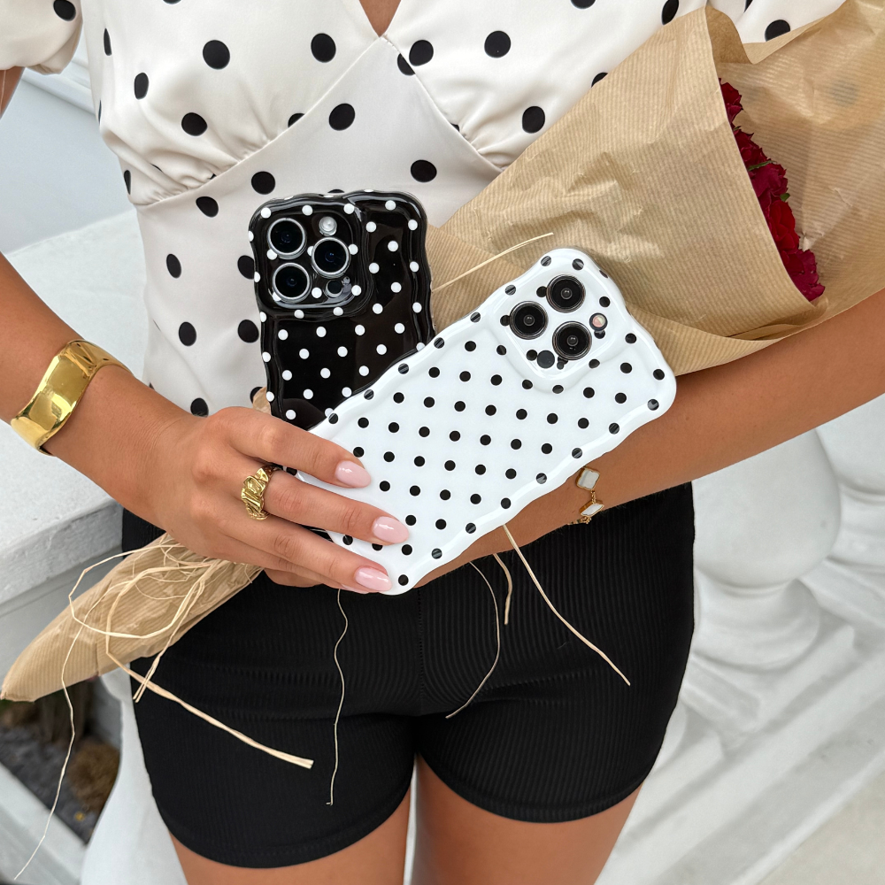 Woman holding a white polka dot wavy phone case and a bouquet, wearing black shorts and a polka dot top.