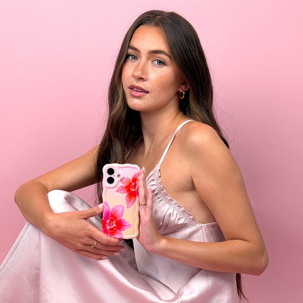 Woman holding a phone with a floral case against a pink background