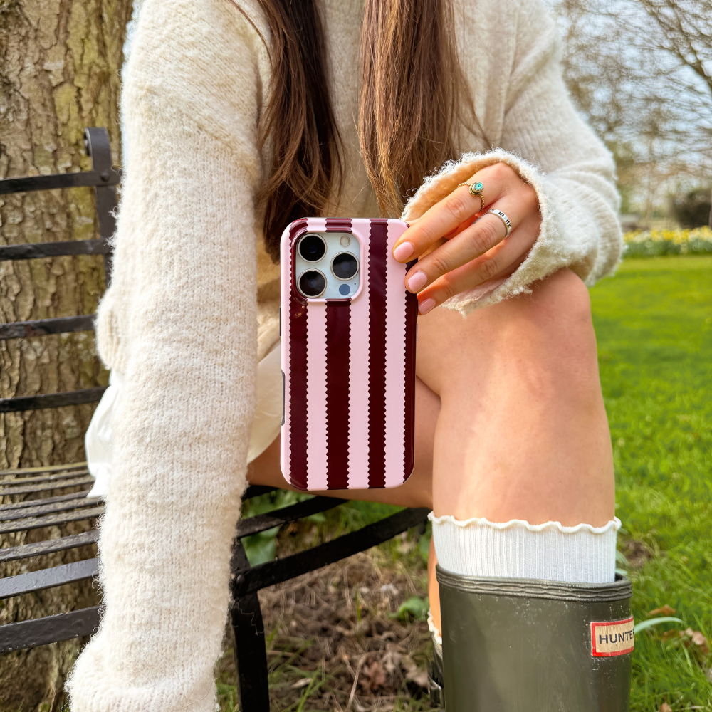 Girl sat in field with blushberry scallop stripes tough phone case in hand wearing cream outfit and wellies