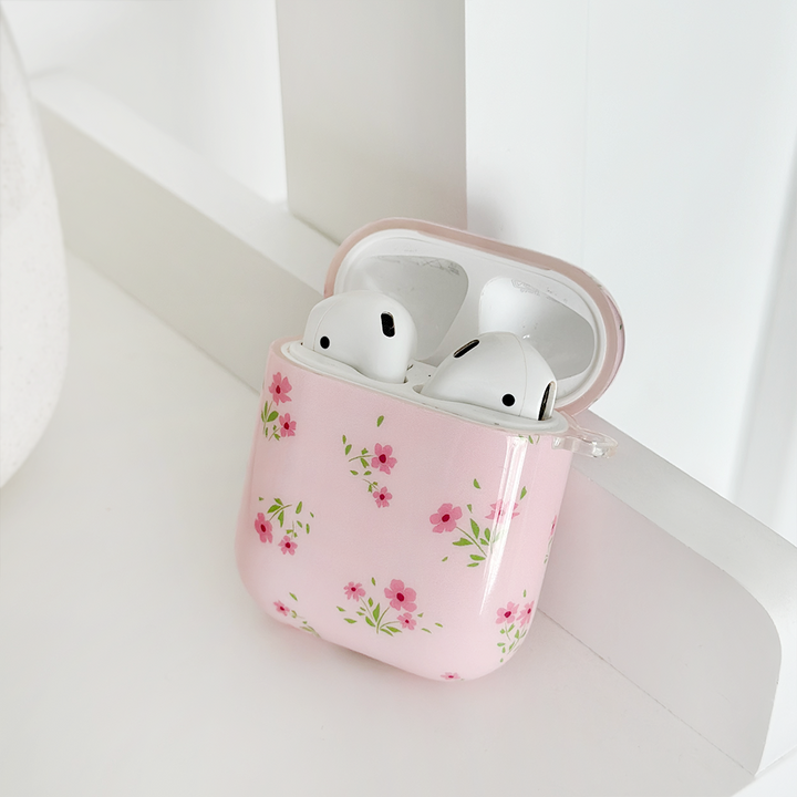 A pair of wireless earbuds inside an open, ditsy floral pink case from Coconut Lane rests on a white surface. The AirPods Case - Ditsy Floral Pink showcases small, colorful flowers printed with IMD Print Technology, giving it a delicate and stylish appearance.