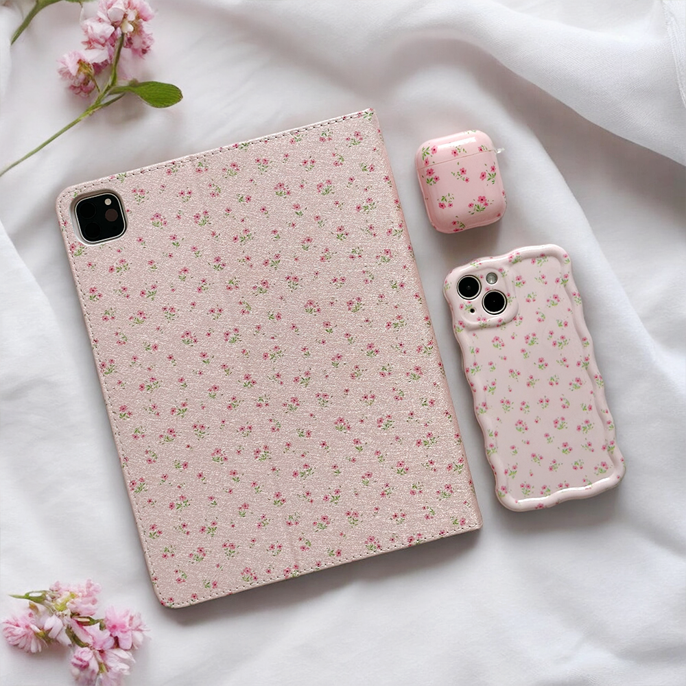 The Ditsy Floral Pink iPad Case by Coconut Lane, along with its matching smartphone case and earbuds case, is showcased on a textured fabric surface. Each accessory features a charming ditsy floral design on a light pink background, with pink flowers scattered around them.