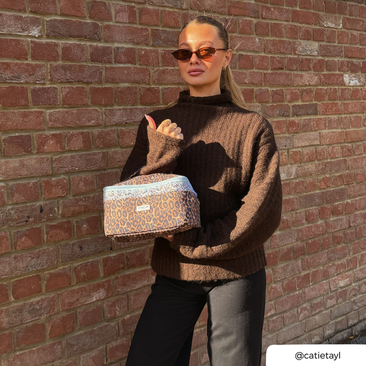 Woman in a brown knit jumper holding the Coconut Lane Leopard Lace vanity case featuring brown leopard print, pale blue lace trim.