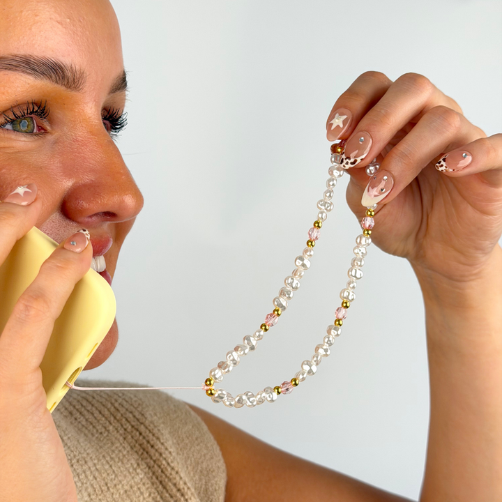 girl smiling on the phone with her pink gold and pink phone strap attached