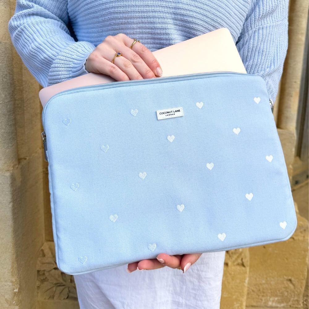 Girl holding a powder blue laptop case with white heart patterns against a stone wall.