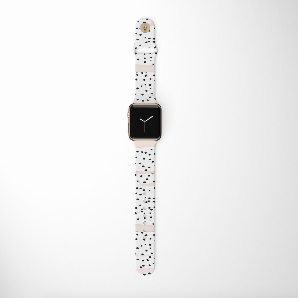 A Coconut Lane Pink Dalmatian Apple Watch Strap is showcased against a plain white background, highlighting its rectangular screen and a white band adorned with black speckles. The watch face displays time with simple hour and minute hands, while the silicone band features beige accents near the lugs and buckle.